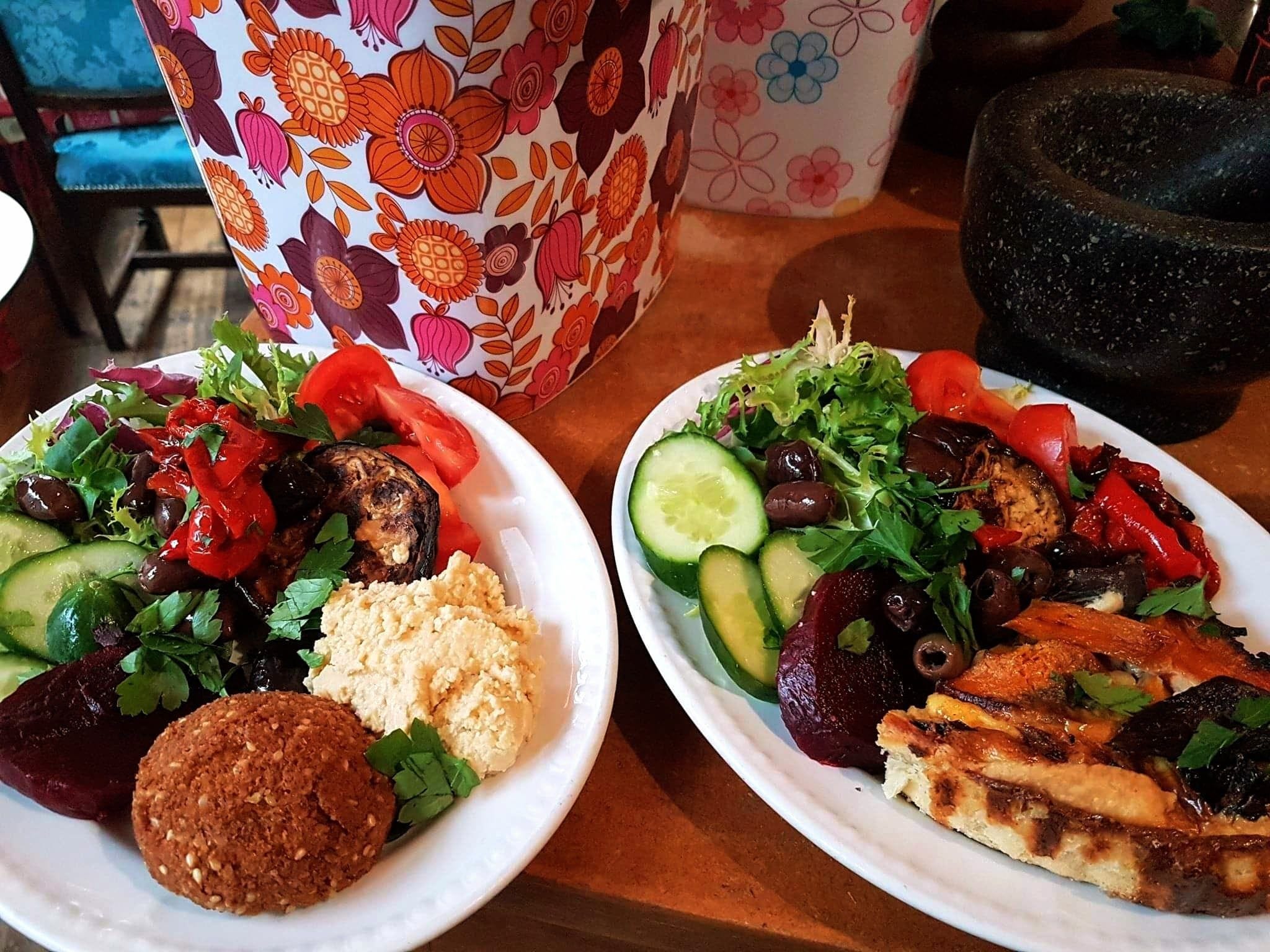 tow plates of salad in front of a colourful 1970s flowery box.
One plate has salad leaves, red peppers, hummus and falafels, the other has salad with quiche