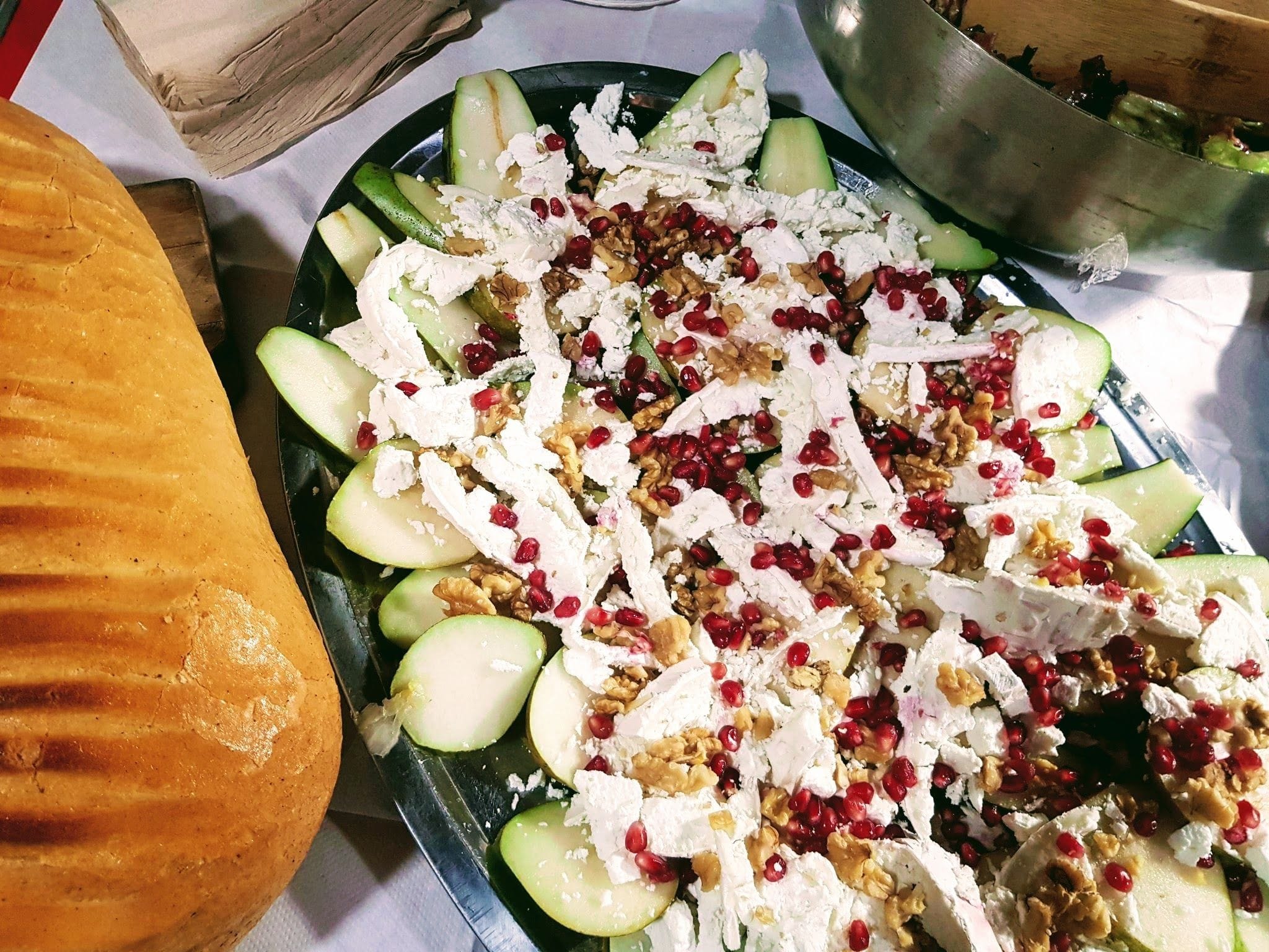 A large platter with slices of pears and goat's cheese garnished with pomegranate seeds. A loaf of bread is next to it