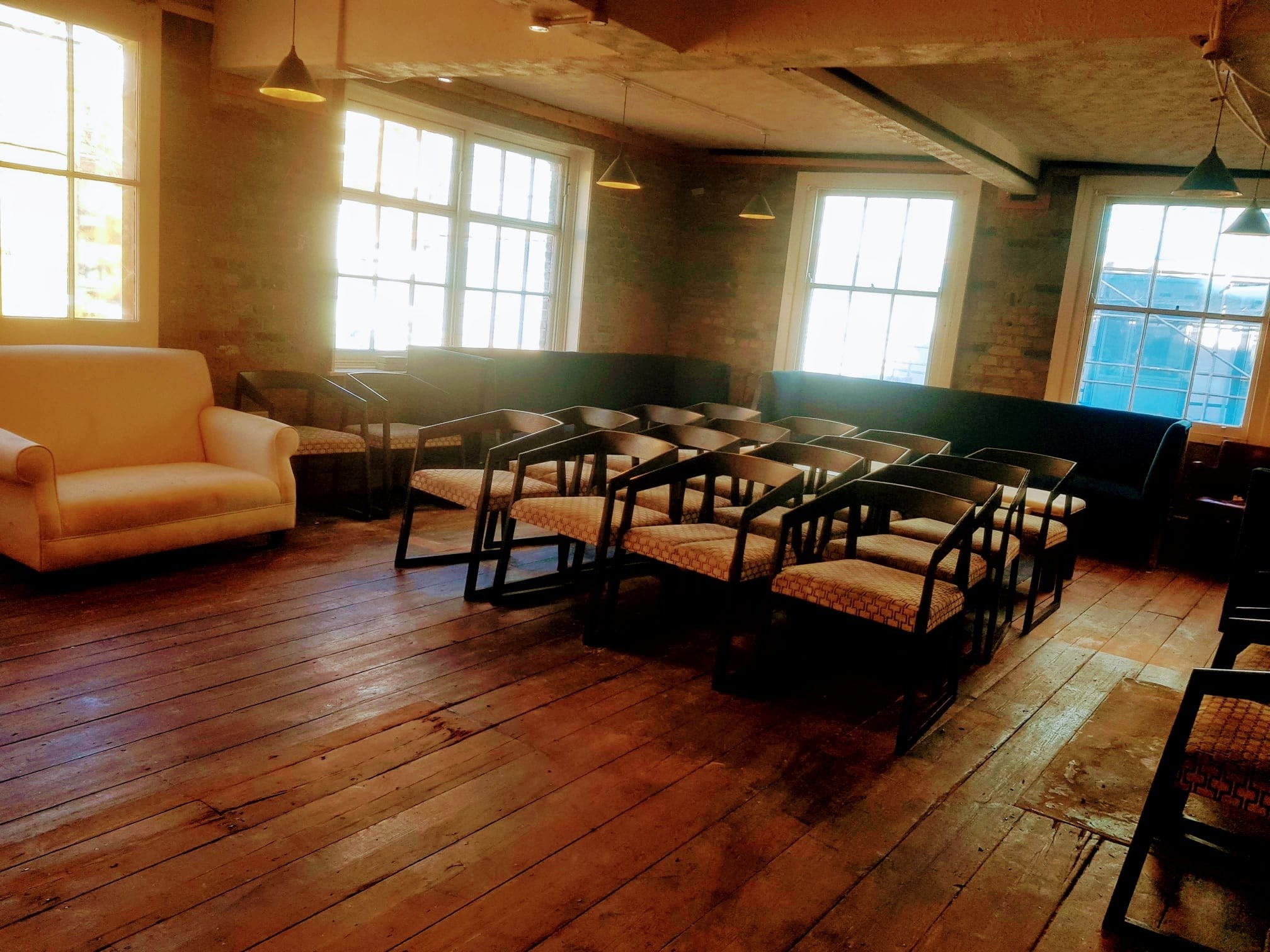 large room with comfortable chairs and sofas, barebrick walls and wooden floors,lots of light thro several windows